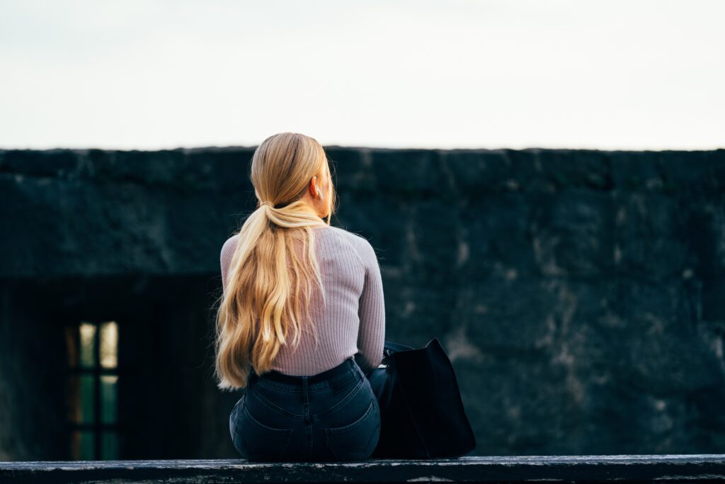 Woman sitting on wall facing away and feeling lost.