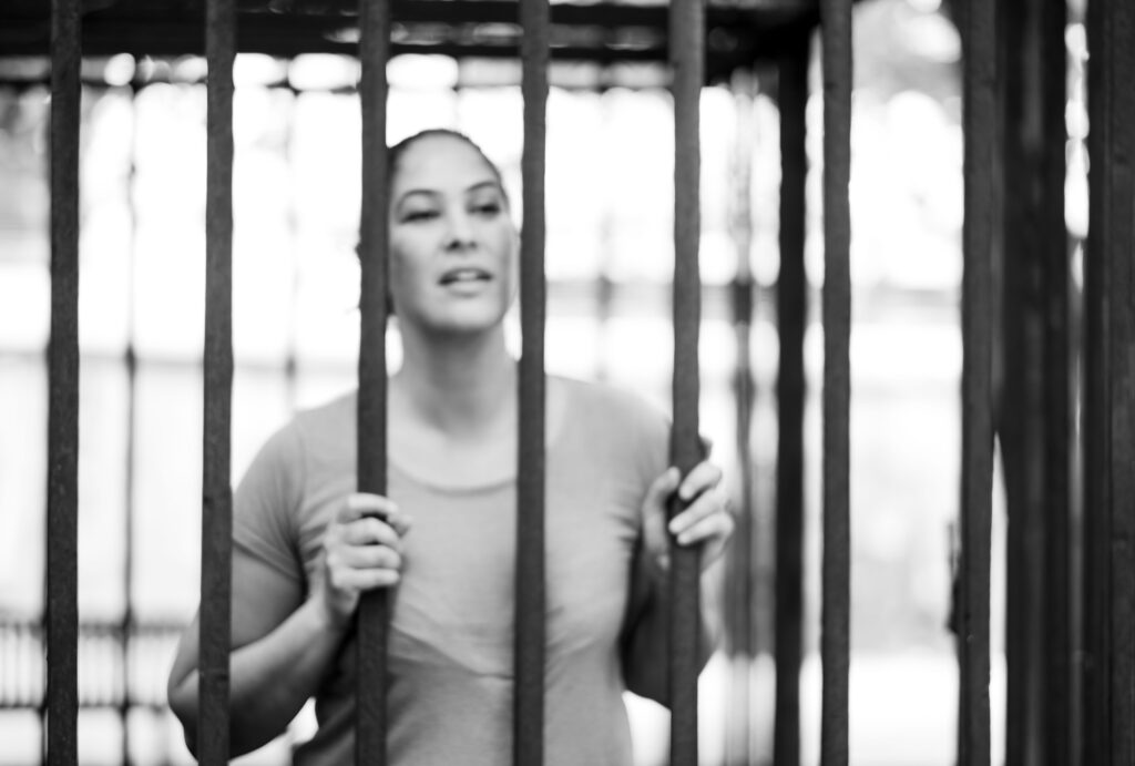 Blurry image of woman looking out through bars. She feels trapped. Her subconscious negative patterns keeping her stuck. 