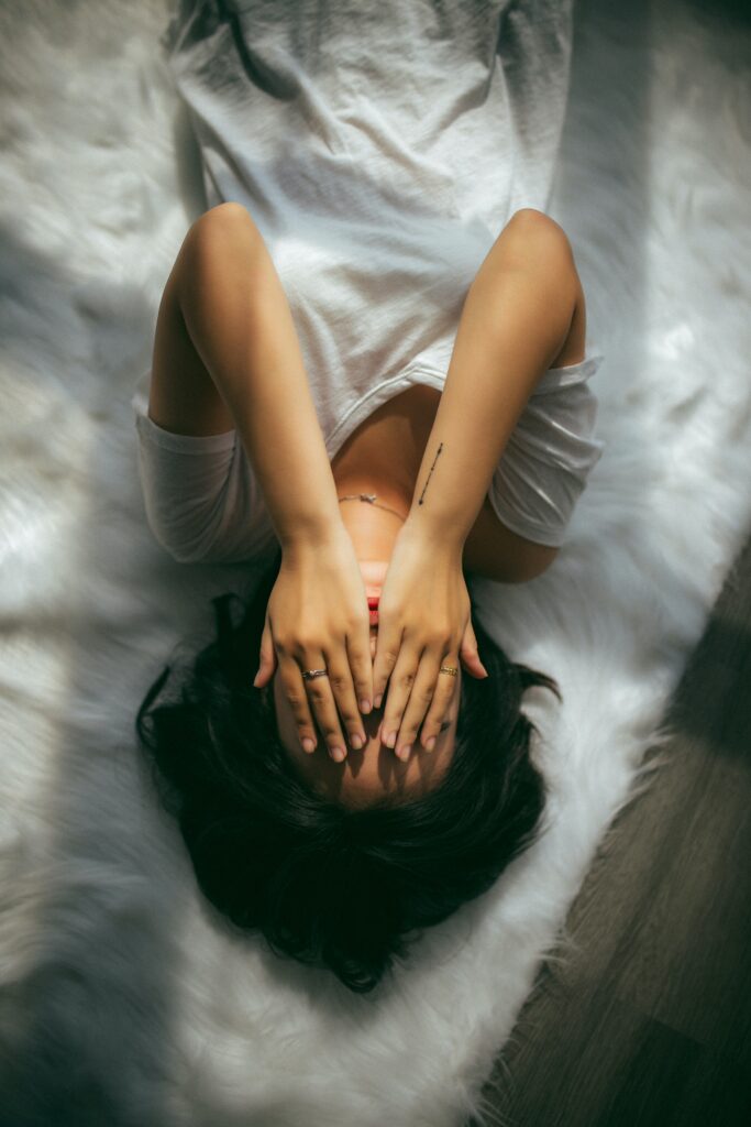 Woman lying on bed with her hands over her face, with too many negatives coming up for her. 
Photo by Anthony Tran on Unsplash