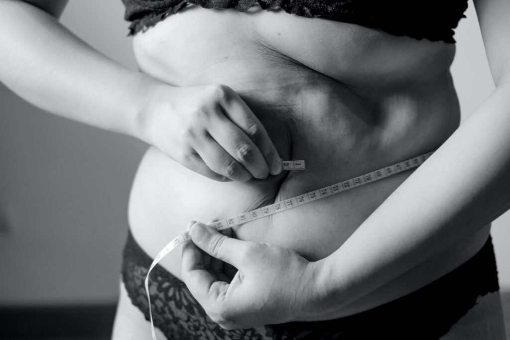 Woman's measuring her waist with measuring tape, wondering if she is too fat to find love. Photo by Fuu J on Unsplash