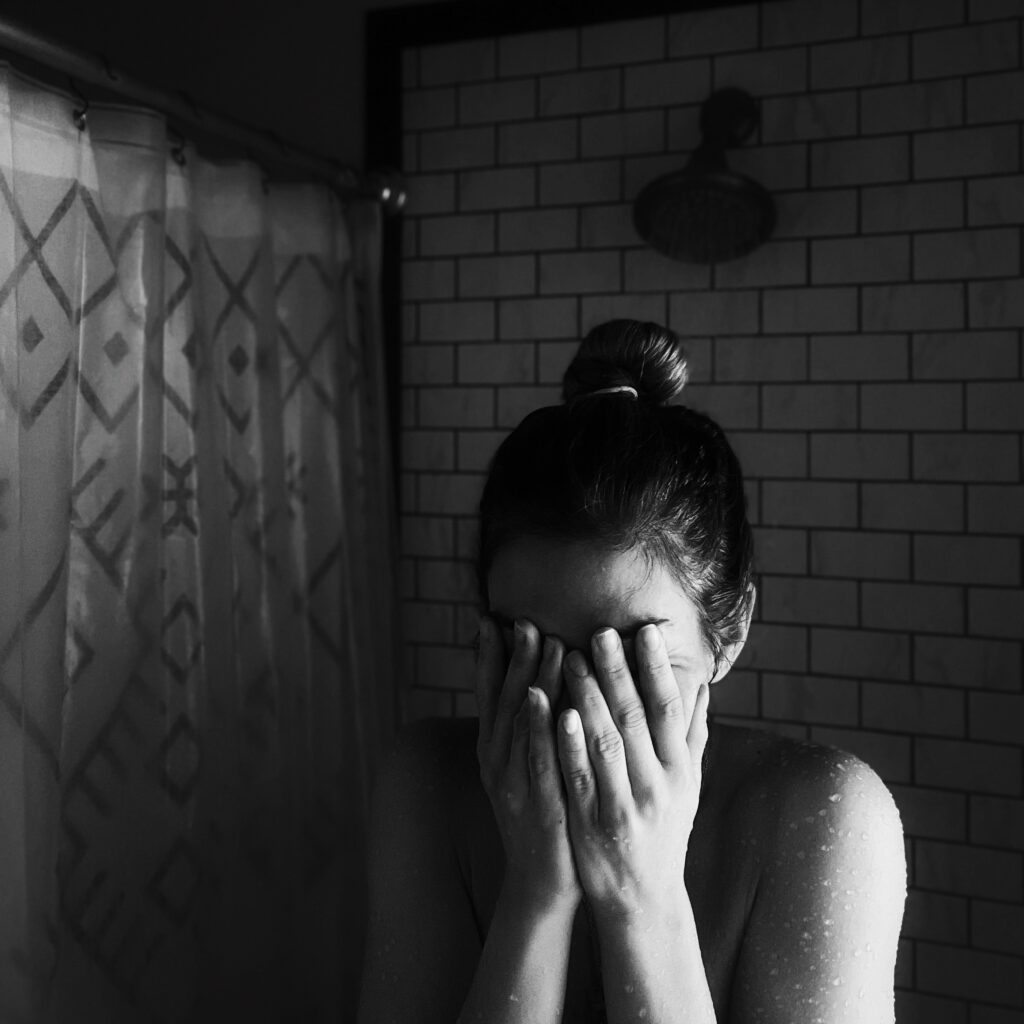 Woman crying in the shower, scared to leave partner. Black and white photo. Photo by Lucia Macedo on Unsplash