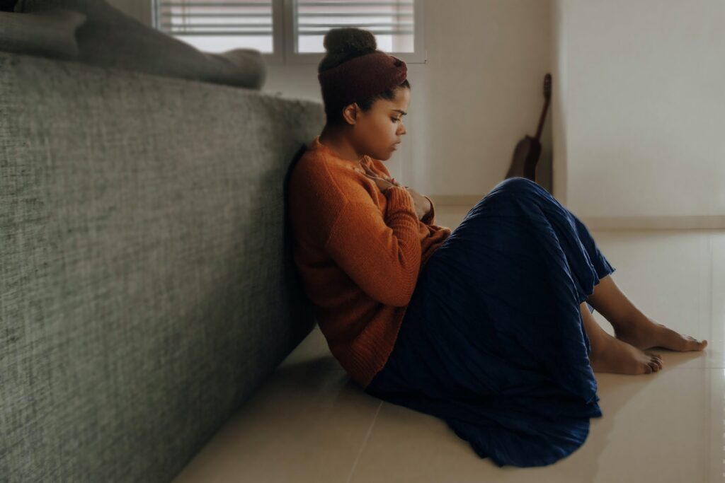 Woman sitting on the floor by her couch. She looks worried. She doesn't want to repeat bad patterns. Photo by Joice Kelly on Unsplash