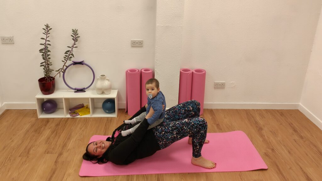 Mum and baby Pilates session. Baby is on mum's lap as she does a shoulder bridge. 