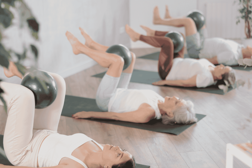 Image of women lying on their back with a small ball between their knees and legs in tabletop, working their pelvic floor muscles. 